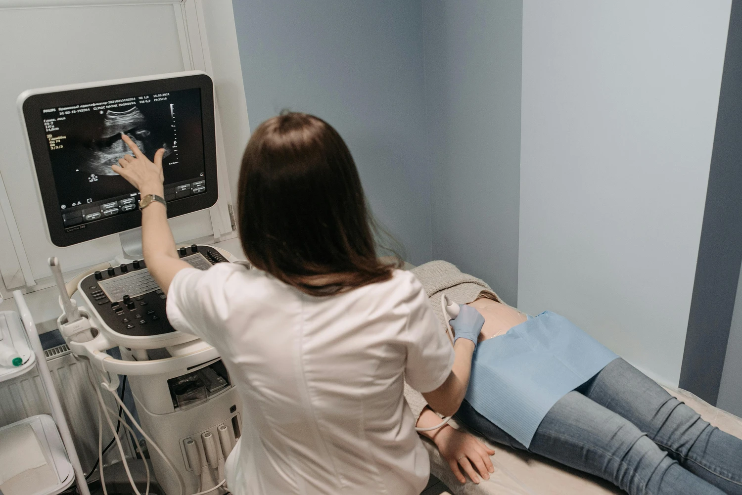 Frauenärztliche Praxis - Fachärztin für Frauenheilkunde und Geburtshilfe - Ärztin führt eine Ultraschalluntersuchung am Bauch einer Patientin durch und zeigt dabei auf den Ultraschallmonitor