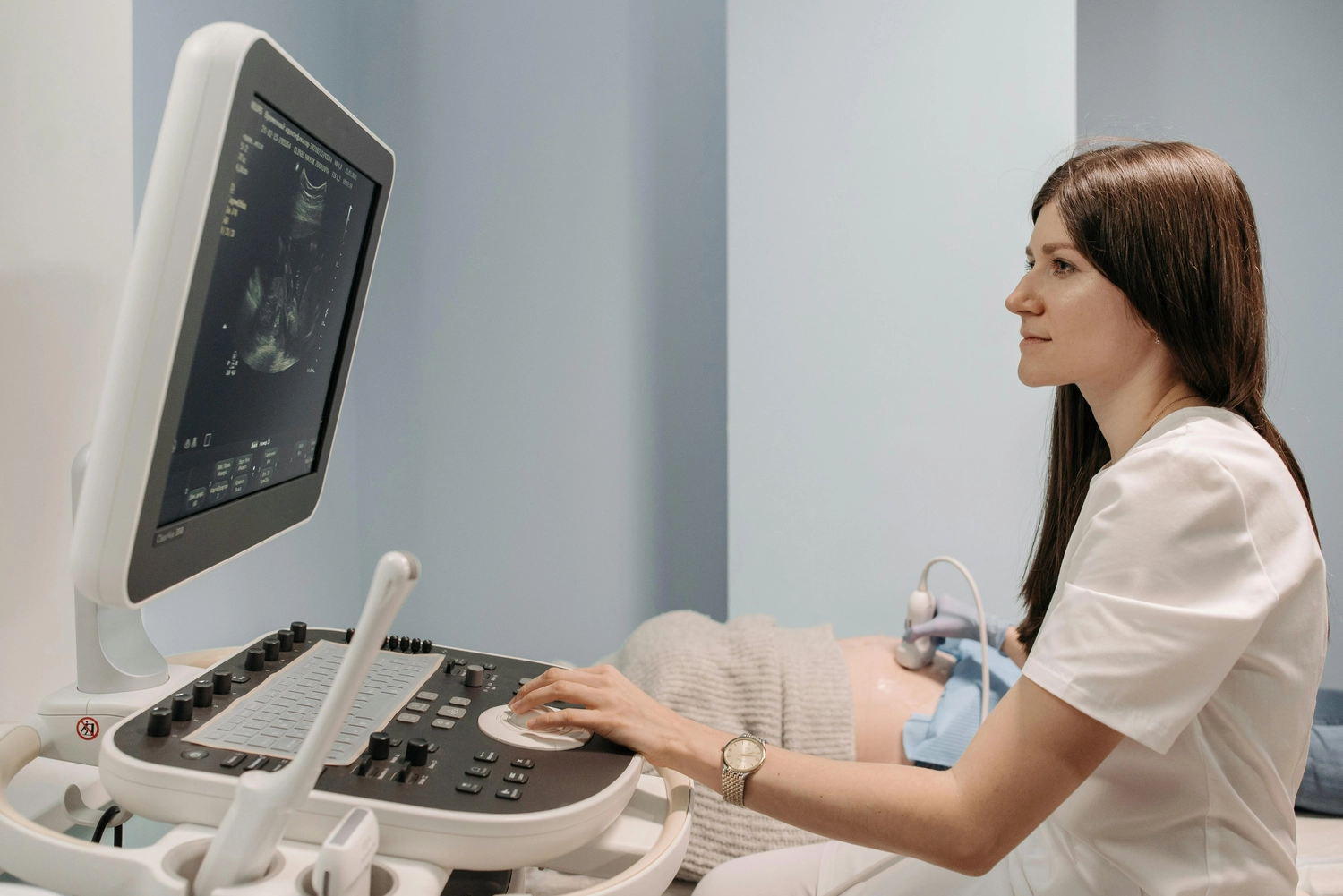 Frauenärztliche Praxis - Fachärztin für Frauenheilkunde und Geburtshilfe - Ärztin führt eine Ultraschalluntersuchung des Abdomens bei einer auf einem Bett liegenden Patientin durch